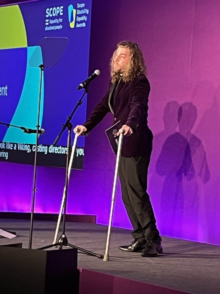 Dan stood on a very purple stage wearing a purple suit jacket talking in to a microphone