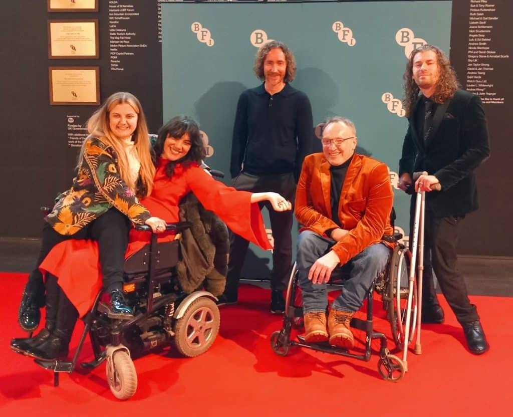 Dan stands in a green suit jacket on a red carpet with fellow members of the Disability Screen Advisory Group