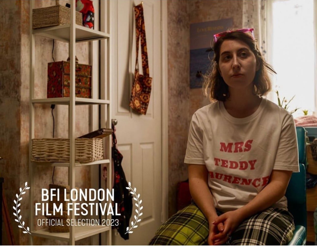 A picture of Rae a young white jewish woman sat in her pyjamas with a BFI London Film Festival selection Logo.